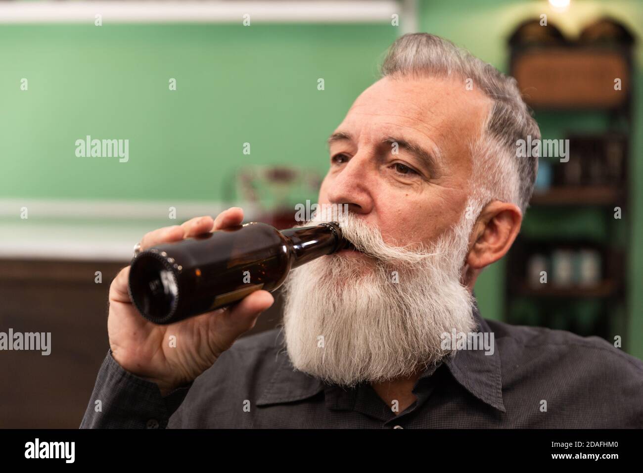 Un homme caucasien plus âgé à barbe, modèle barbu, dans un bar rétro hipster, boit une bouteille de bière, photo portrait. Banque D'Images