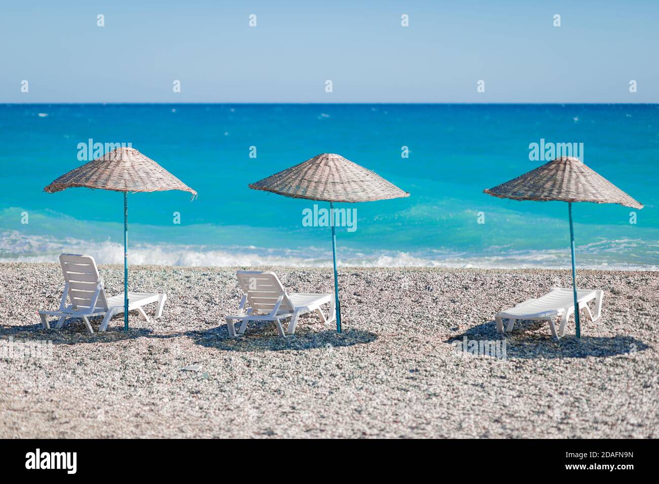 Très belle vue sur la plage avec des galets et l'océan bleu ou la mer azur avec des chaises longues blanches et des parasols en osier. Le concept d'un postc Banque D'Images