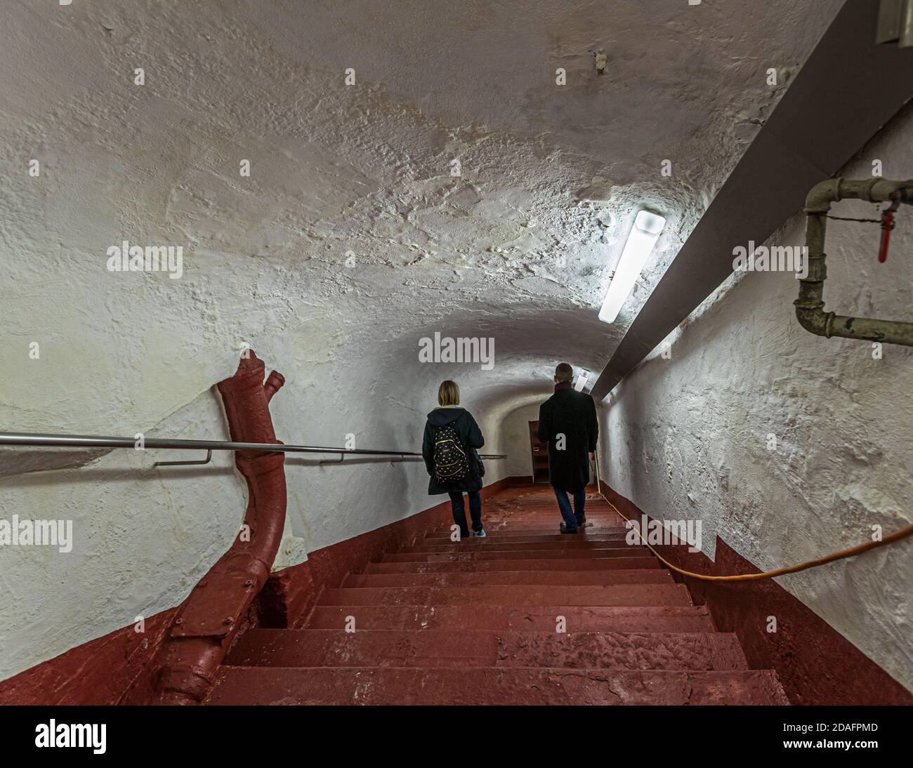 Deux visiteurs descendent les marches en pierre rouge menant à la cave creusée dans la roche du Stephansberg avec Matthias Trum, qui dirige la brasserie de bière fumée Heller-Bräu Schlenkerla depuis 2003, à Bamberg, en Bavière, en Allemagne. Trum est également considéré comme un historien de la bière, ce qui l’aide à préserver les 600 années d’histoire de sa propre brasserie. Banque D'Images
