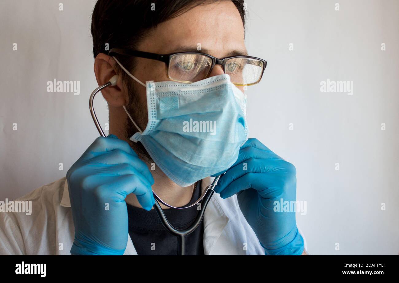 Un jeune beau médecin portant des lunettes et un masque médical met sur un stéthoscope tout en se préparant à un examen du patient. Banque D'Images