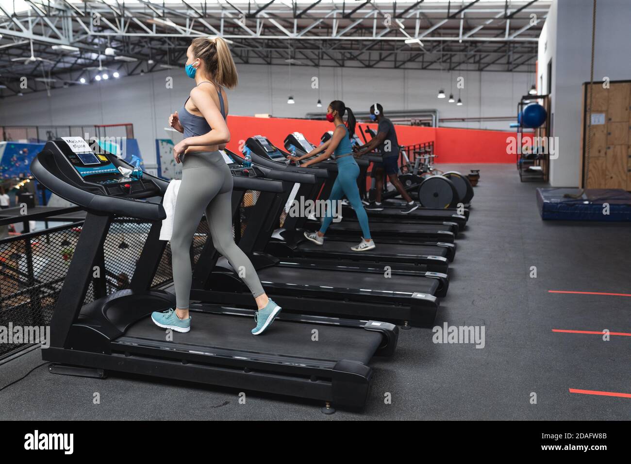 Ajuster la femme caucasienne portant un masque de course sur tapis roulant faisant entraînement cardio dans la salle de gym Banque D'Images