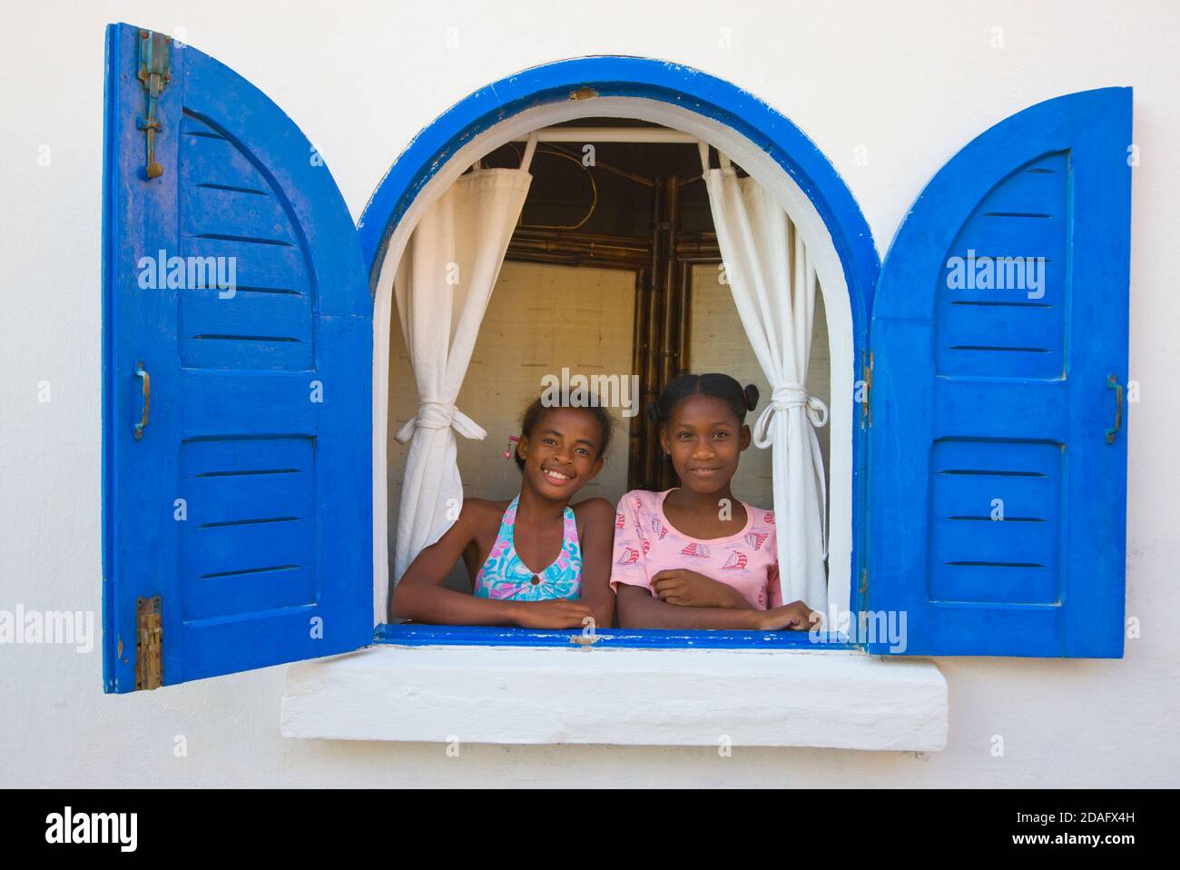 Deux filles par fenêtre avec volets bleus, Morondava, Madagascar Banque D'Images