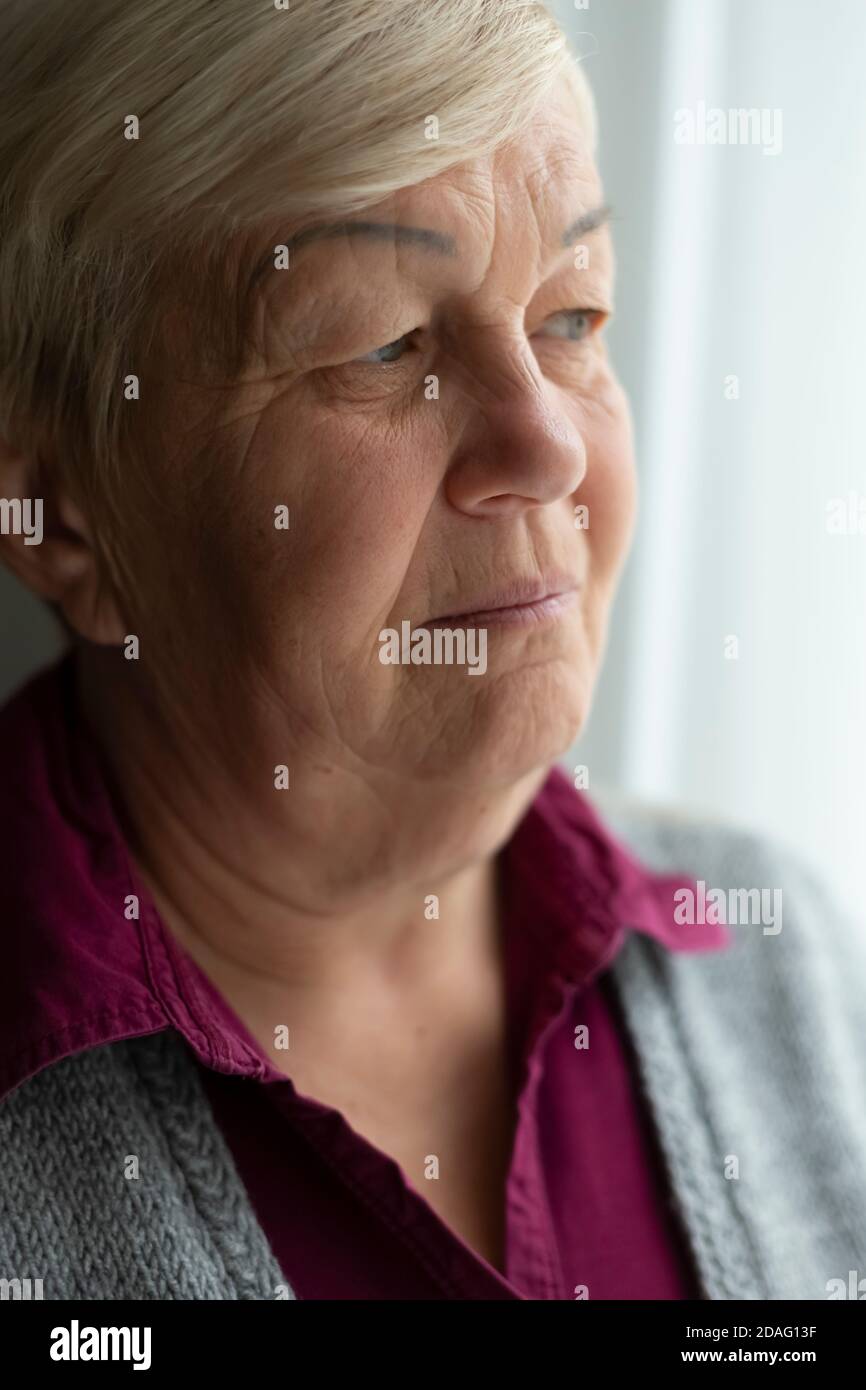 Visage d'une femme âgée qui regarde par la fenêtre. Portrait en gros plan de la vieille femme triste. Banque D'Images