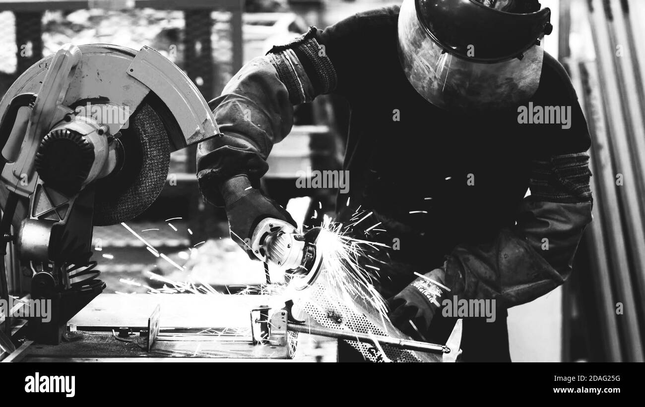 Ouvrier de l'industrie lourde coupant l'acier avec une meuleuse dans la fabrication industrielle, noir et blanc Banque D'Images