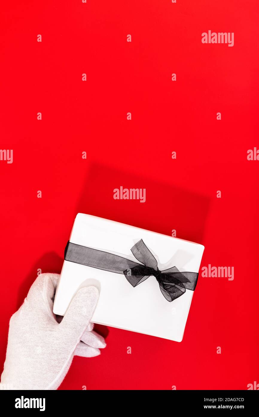 Le Père Noël avec des mains gantées tenant un cadeau de Noël sur fond rouge. Copier l'espace. Banque D'Images