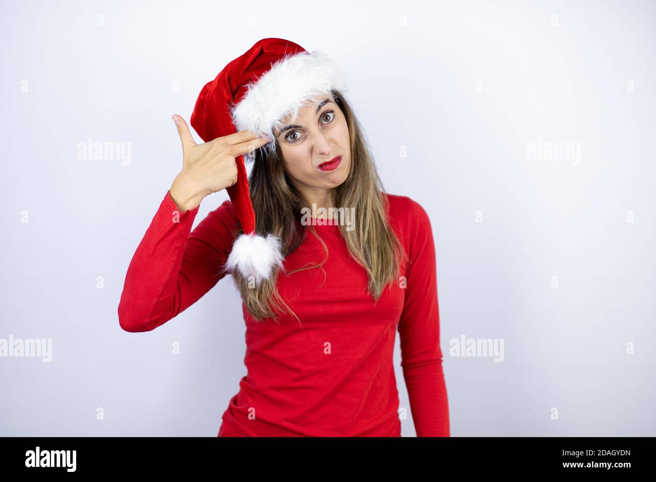 Jeune belle femme portant un chapeau de père Noël sur fond blanc de tir et de tuer se pointant la main et les doigts à la tête comme un fusil, suicide gestu Banque D'Images