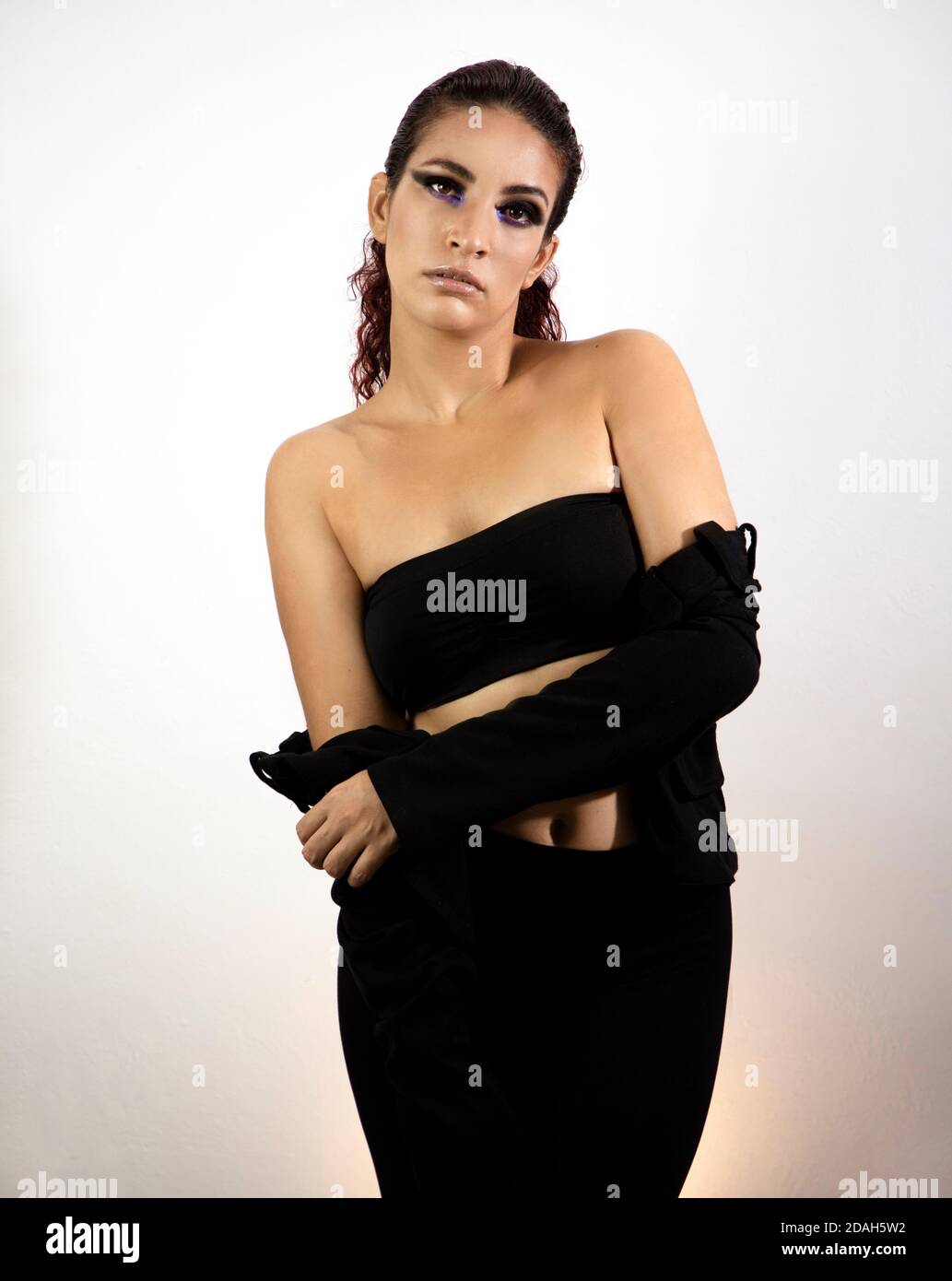 Jeune fille posant pour une séance photo vêtue de noir avec une veste ouverte et les épaules nues et les cheveux rouges. Banque D'Images