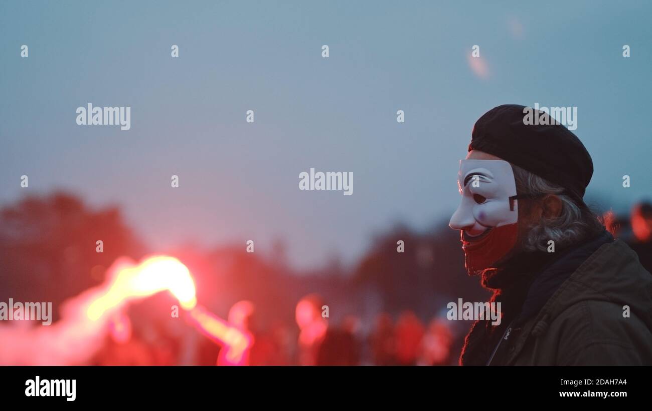 Varsovie, Pologne 11.11.2020 - 102e anniversaire du jour de l'indépendance de la Pologne. Homme avec le masque de visage dans les couleurs de glag polonais debout dans l'gropu de personnes brûlant des fusées rouges. Photo de haute qualité Banque D'Images
