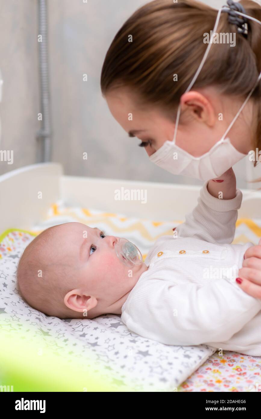 Une femme dans un masque de protection médicale prend soin de son bébé. Protection prophylactique du coronavirus et du covid-19 pendant une pandémie. Banque D'Images