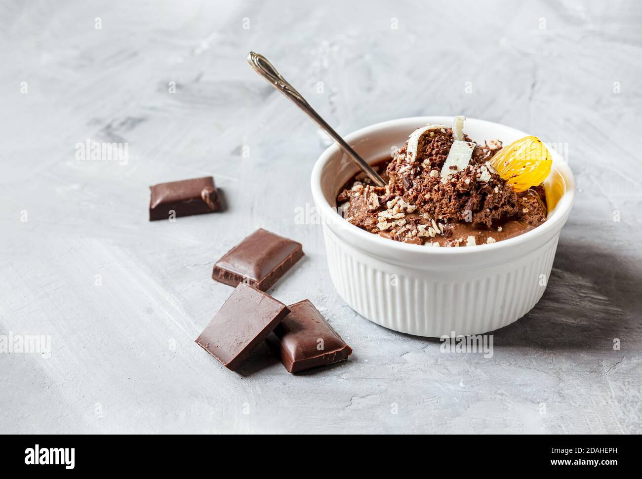 Mousse au chocolat garnie d'un coin de mandarine et de chocolat blanc copeaux dans un bol blanc et morceaux de chocolat sur un table grise Banque D'Images