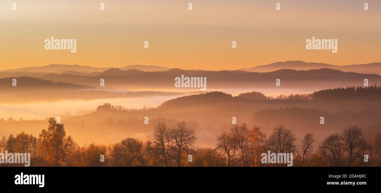 coucher de soleil dans les montagnes - paysage vallonné avec des prairies et des forêts dans une brume, dans un ciel jaune et orange Banque D'Images