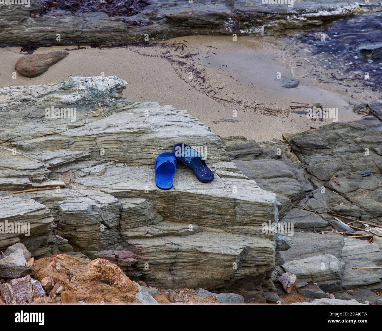 Paire impaire. Copier l'espace. Une mauvaise paire de sandales de plage en plastique bleu laissées sur un rocher par le bord de mer. Image de stock. Banque D'Images