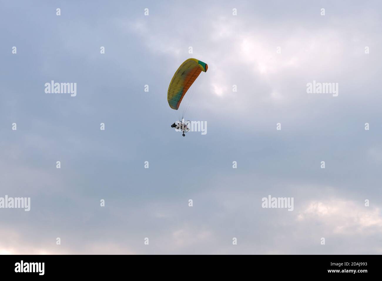 Un parapente motorisé en tandem vole dans le ciel nuageux du soir avec un pilote et un passager. Banque D'Images