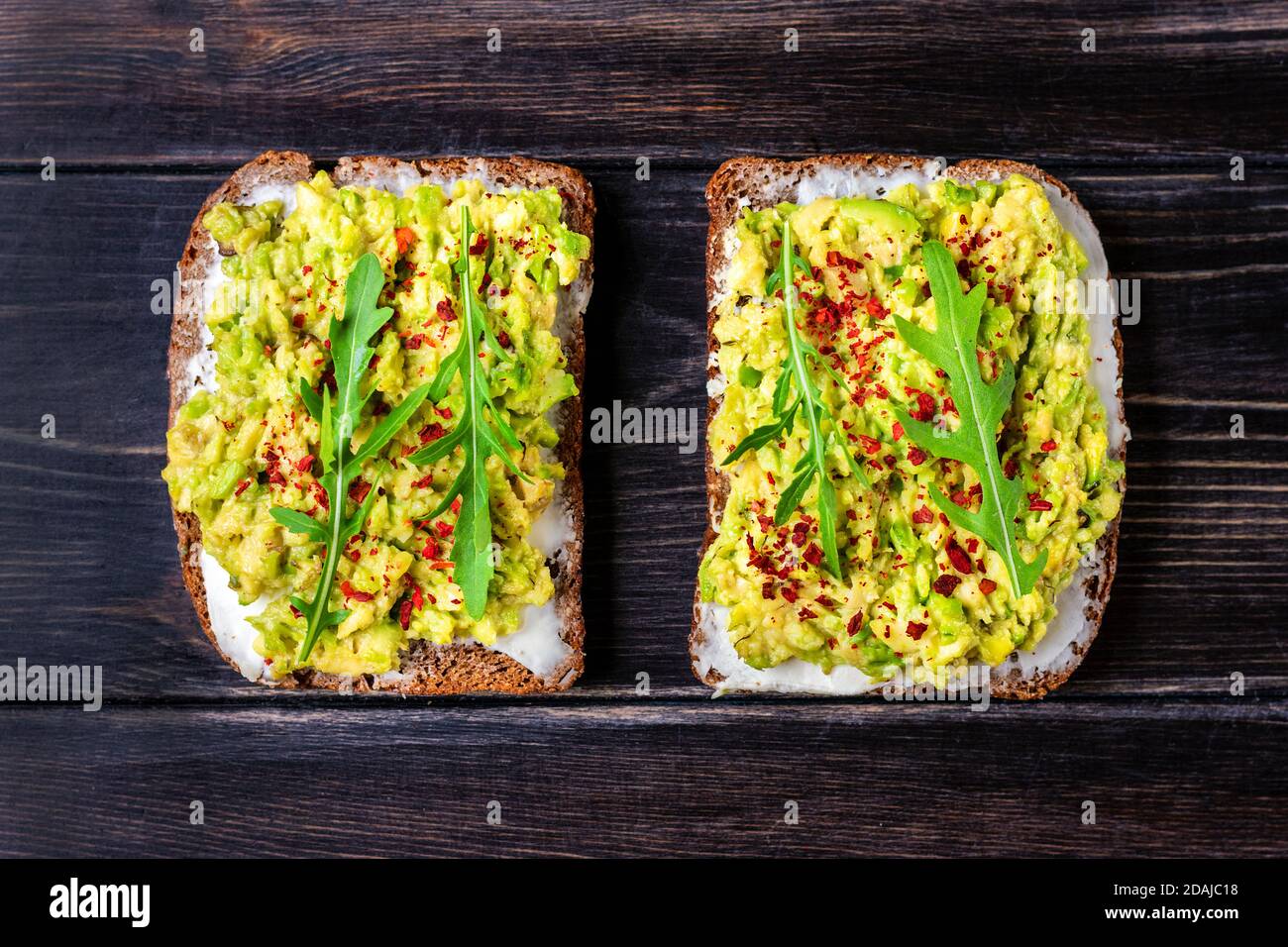 Set sandwiches pour le petit déjeuner - tranche de pain noir de grain entier, fromage à la crème, guakomole, garni d'arugula, paprika sur table en bois vue du dessus plat Banque D'Images