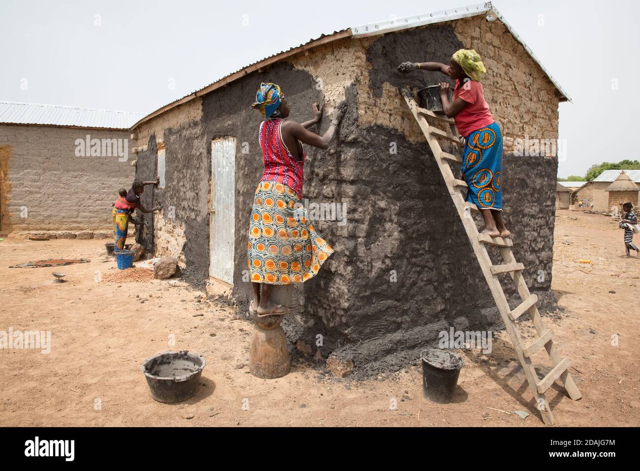 Delaba Koro, village à 60 kms de Selingue, Mali, le 27 avril 2015; ce village a entraîné de nombreuses personnes déplacées par le barrage. Les femmes scellent les murs de leur maison contre les pluies à venir avec un mélange liquide de boue et de fumier animal. Rokia Camara, 18 ans, est au sommet de l'échelle. Banque D'Images