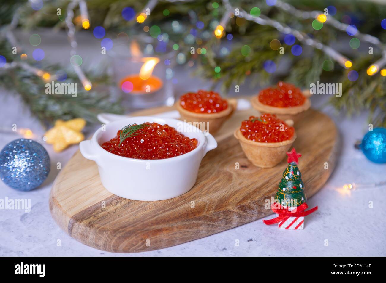 Caviar rouge (caviar de saumon) dans un bol blanc sur une planche de bois. En arrière-plan sont des tartelettes avec caviar, branches d'arbre de Noël, jouets, bougie et bo Banque D'Images