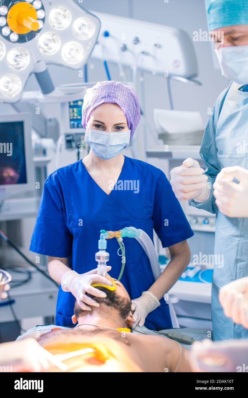 Dans la salle d'opération de l'hôpital, l'anesthésiologiste applique le masque d'anesthésie à un patient, les assistants désinfectent avec l'iode lieu d'incision, les chirurgiens Banque D'Images