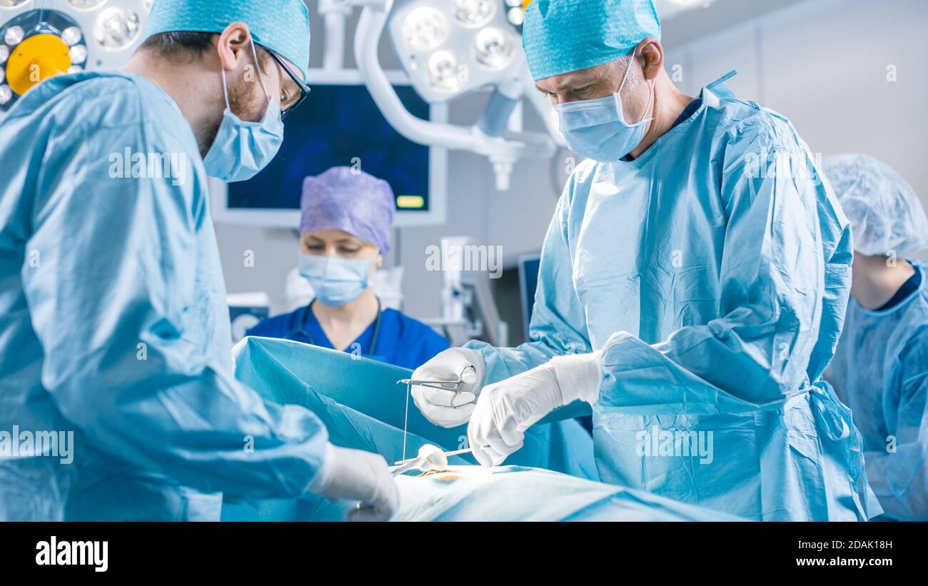 Équipe diversifiée de chirurgiens professionnels, d'assistants et d'infirmières effectuant une chirurgie invasive sur un patient dans la salle d'opération de l'hôpital. Les chirurgiens parlent et Banque D'Images