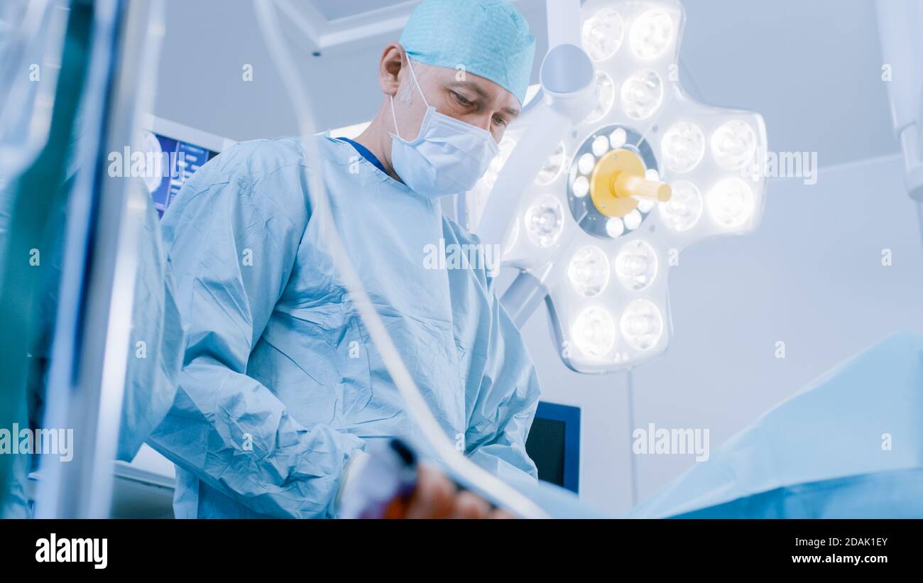 Prise de vue à angle bas en salle d'opération, l'assistant transmet l'instrument à un chirurgien en chef pendant la chirurgie invasive. Médecins professionnels effectuant la chirurgie dans Banque D'Images