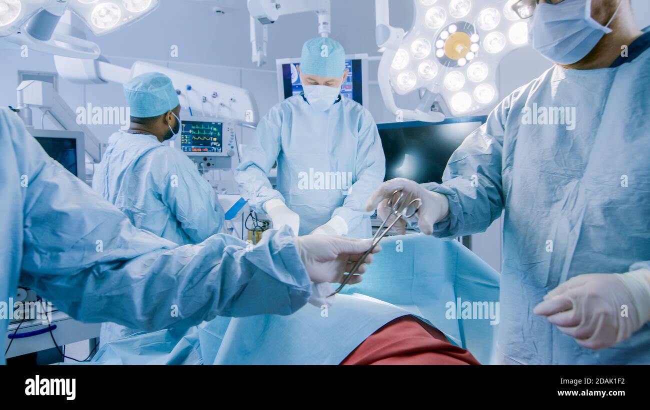 Équipe diversifiée de chirurgiens professionnels effectuant une chirurgie invasive sur un patient dans la salle d'opération de l'hôpital. L'infirmière transmet l'instrument à un chef Banque D'Images