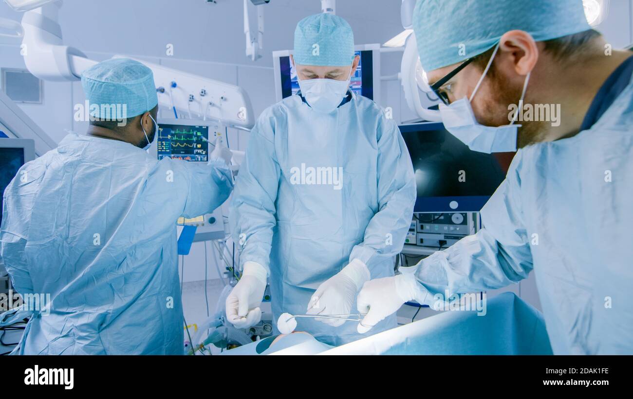Équipe diversifiée de chirurgiens professionnels effectuant une chirurgie invasive sur un patient dans la salle d'opération de l'hôpital. L'anesthésiste surveille les paramètres vitaux Banque D'Images
