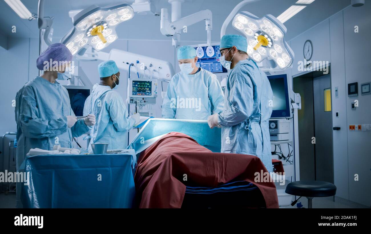 Équipe diversifiée de chirurgiens professionnels effectuant une chirurgie invasive sur un patient dans la salle d'opération de l'hôpital. L'infirmière remet les instruments au chirurgien Banque D'Images