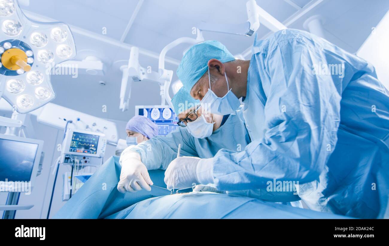 Équipe diversifiée de chirurgiens professionnels, d'assistants et d'infirmières effectuant une chirurgie invasive sur un patient dans la salle d'opération de l'hôpital. Les chirurgiens parlent et Banque D'Images