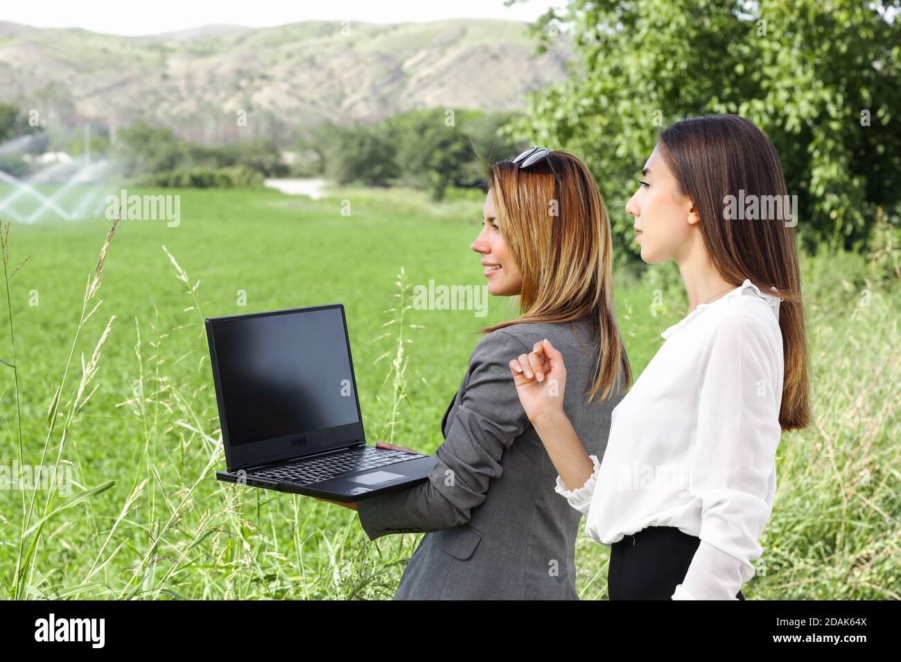 Femmes d'affaires avec un ordinateur portable dans un champ avec système d'irrigation agricole. Arroseurs d'eau en arrière-plan. Banque D'Images