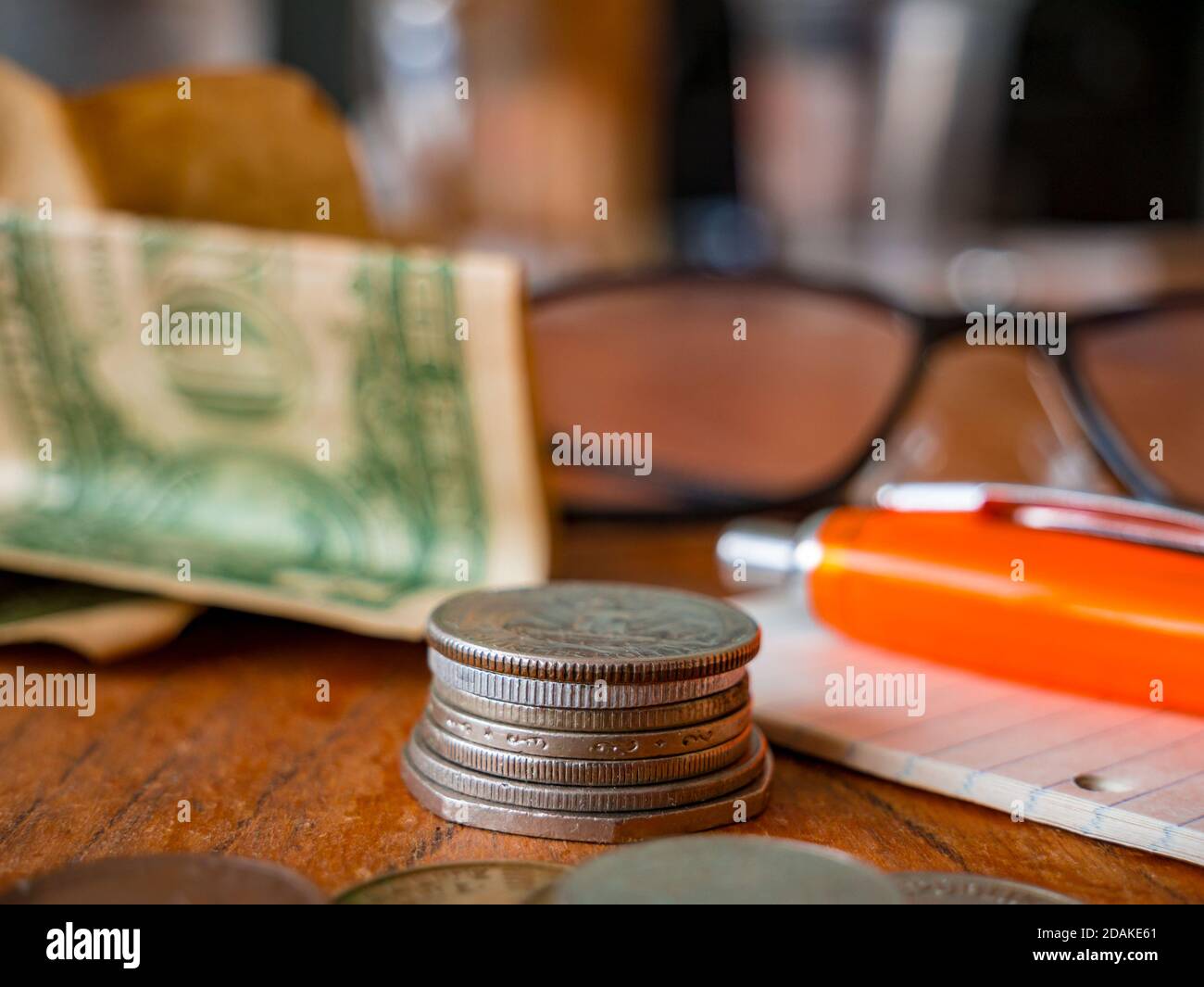 Pile de pièces, floue pliée un billet de dollar américain, un bloc-notes avec un stylo et des lunettes en arrière-plan et une pile de pièces au premier plan. Banque D'Images