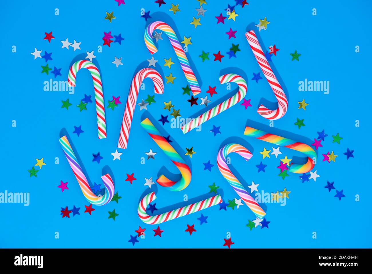 Fond de Noël avec différents confettis de canne à sucre et d'étoiles sur le bleu. Cannes arc-en-ciel et glaçons traditionnels. Banque D'Images