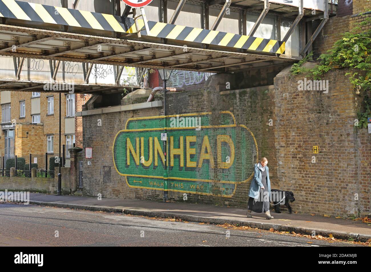 Une femme marche son chien devant le panneau Painted Nunhead à la gare de Nunhead, dans le sud-est de Londres, au Royaume-Uni. En dessous du pont ferroviaire sur Gibbon Road. Banque D'Images