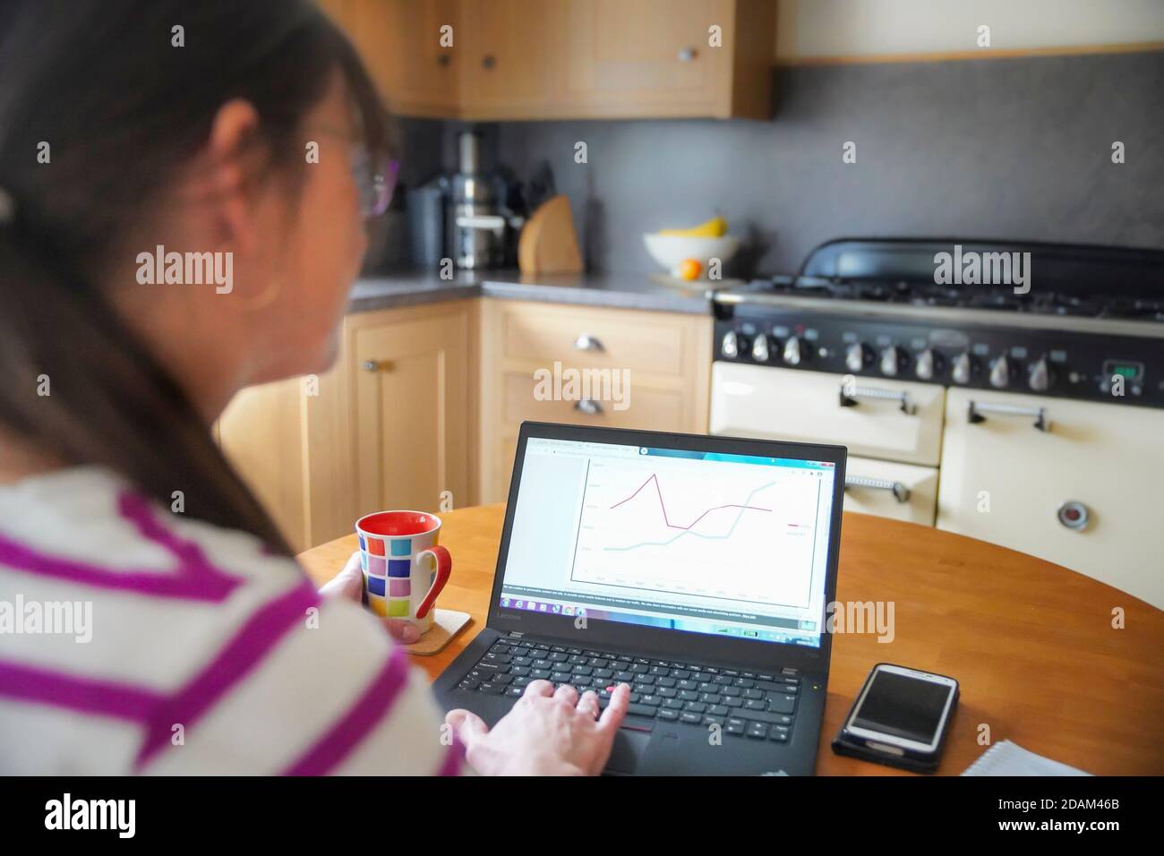 Vue latérale d'une femme isolée à la maison, travaillant sur un ordinateur portable dans sa cuisine. Faire comme d'habitude pendant les mois de confinement de la pandémie de 2020. Banque D'Images
