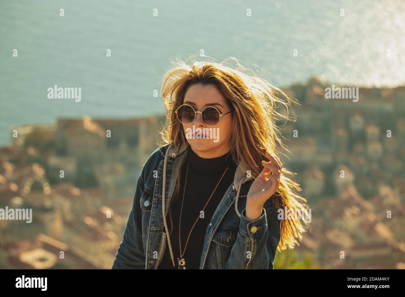 Jolie brune avec des lunettes de soleil jouant avec ses cheveux comme le  soleil se coucher au-dessus de la ville de Dubrovnik en arrière-plan.  Portrait dans l'heure d'or, c Photo Stock -