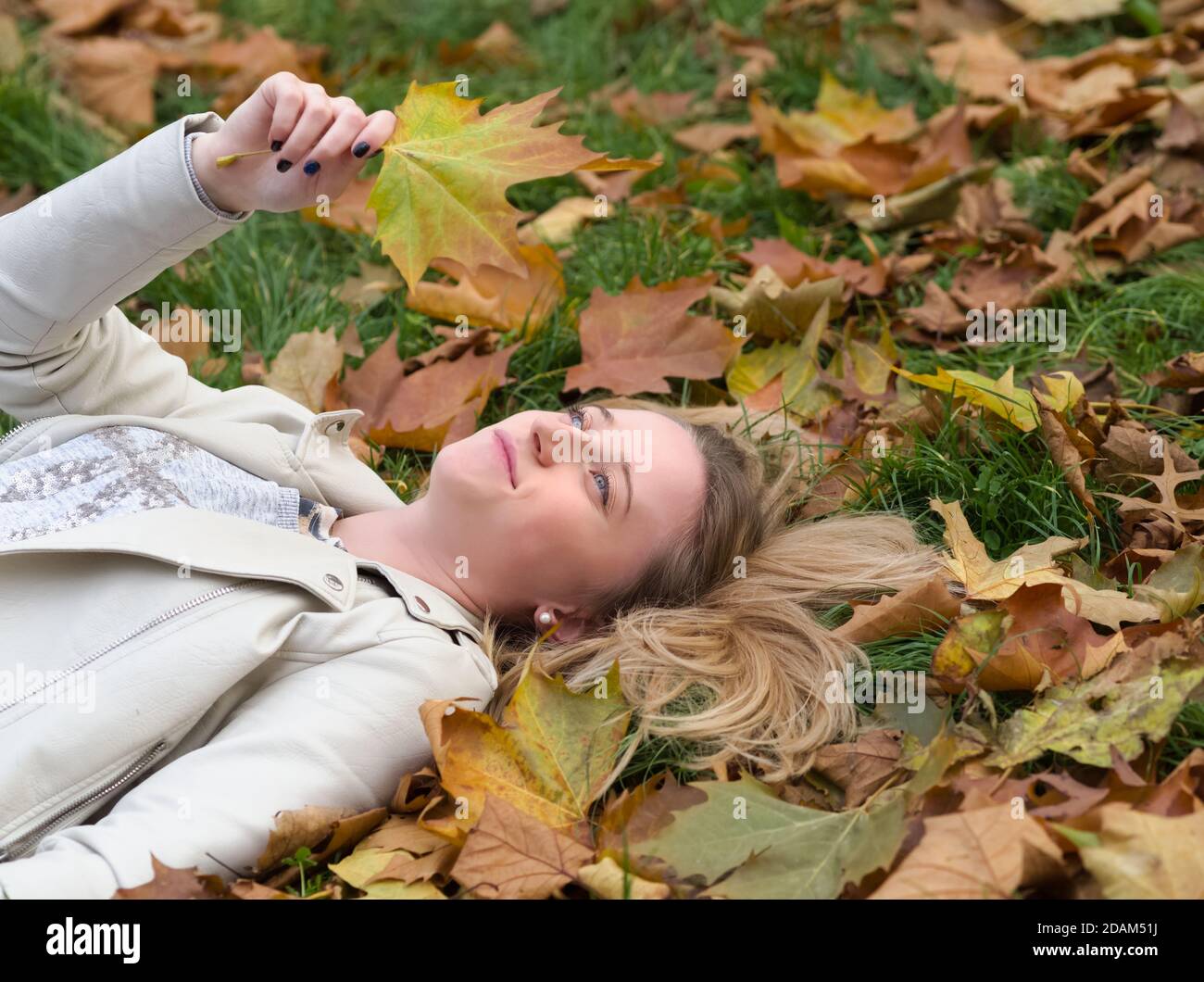 Jeune belle femme Blonde pond qui pond dans l'herbe en automne Parc au milieu des feuilles d'érable Banque D'Images