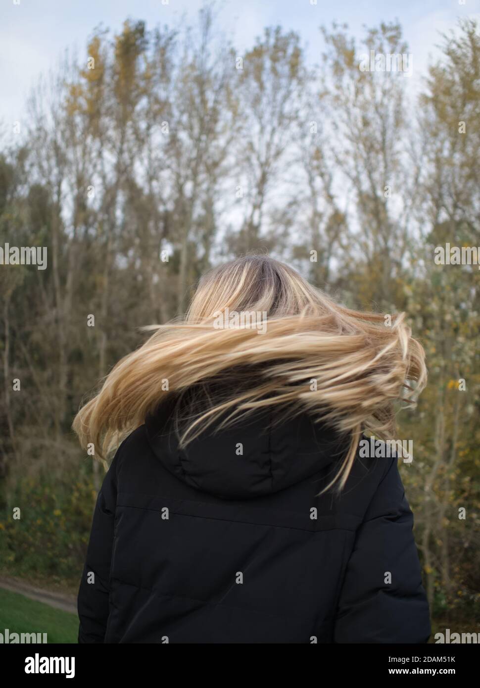 Vue arrière d'une jeune femme qui lance sa longue Blonde Cheveux dans le parc d'automne Banque D'Images