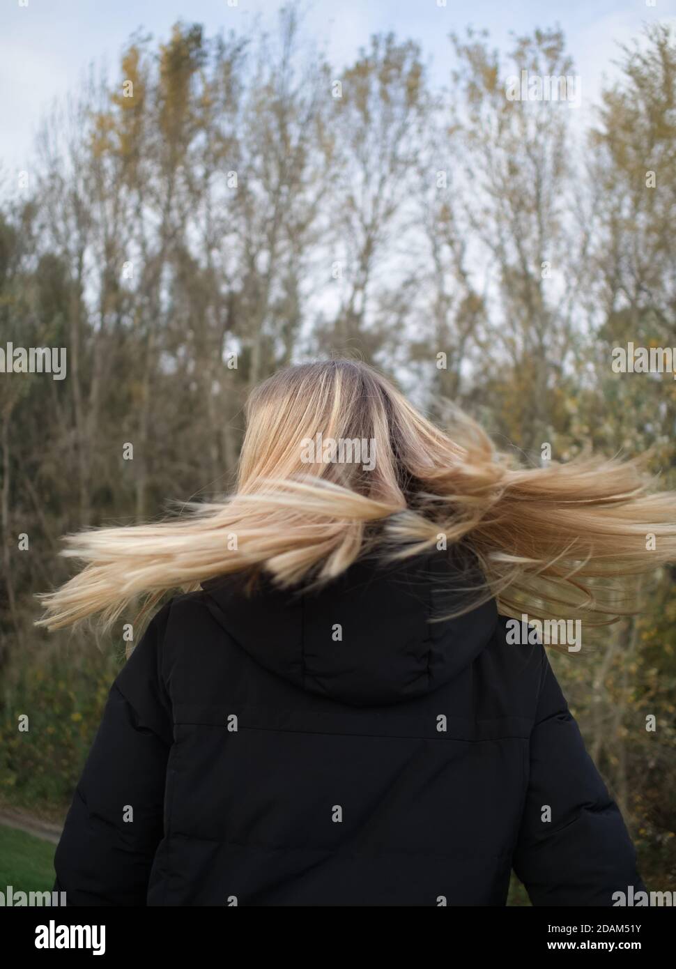 Vue arrière d'une jeune femme qui lance sa longue Blonde Cheveux dans le parc d'automne Banque D'Images