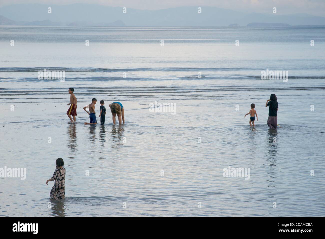 Le ferry pour passagers indonésiens KMP KORMOMOLIN au large de la côte de Lombok, en Indonésie. Indonésiens à la recherche de mollusques et crustacés sur la rive sablonneuse. Pringgabaya, Lombok est Banque D'Images