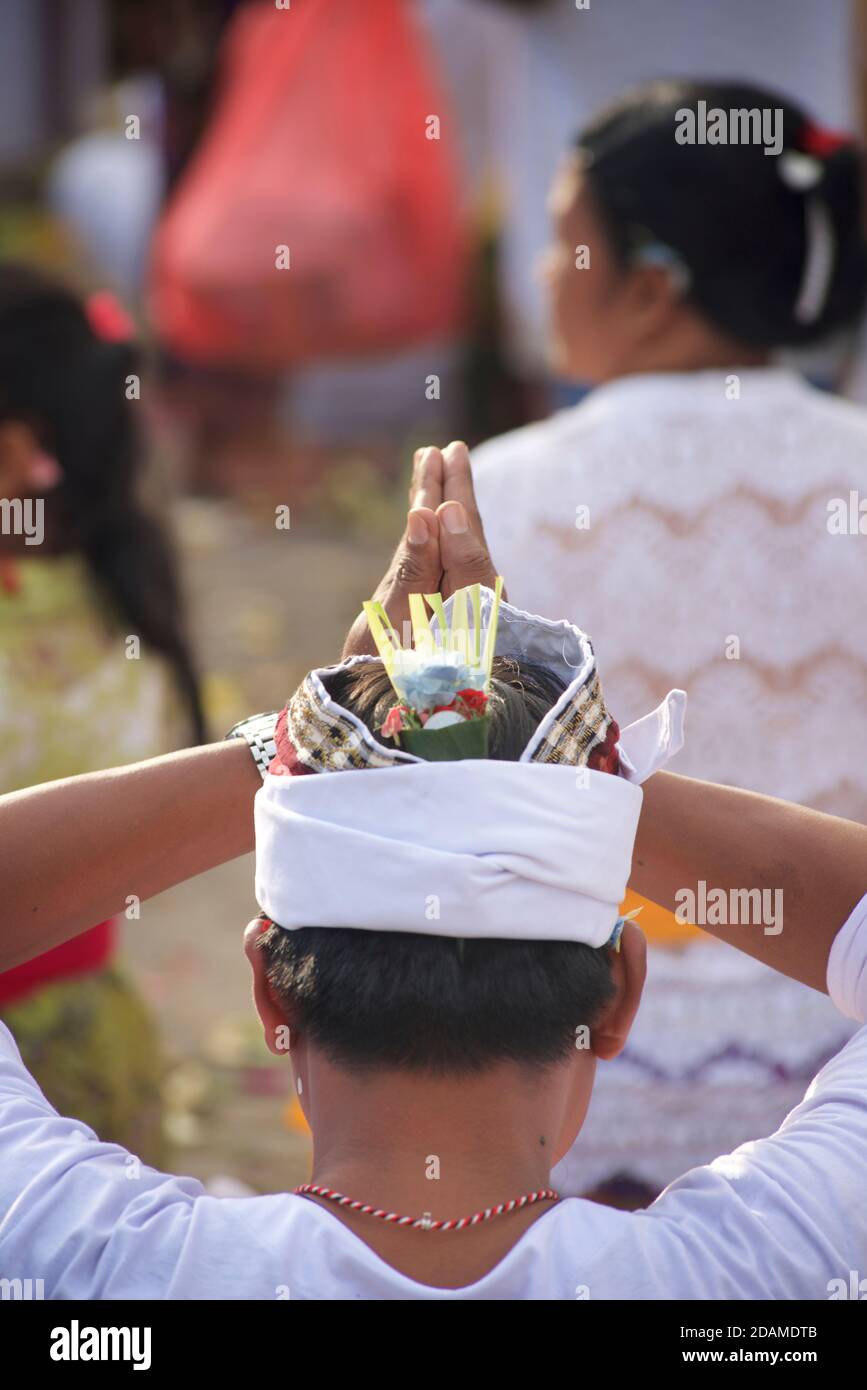 Homme balinais en tenue traditionnelle priant avec ses mains au-dessus de sa tête. Célébrations de Galungan, temple de Sakenan, Bali, Indonésie Banque D'Images
