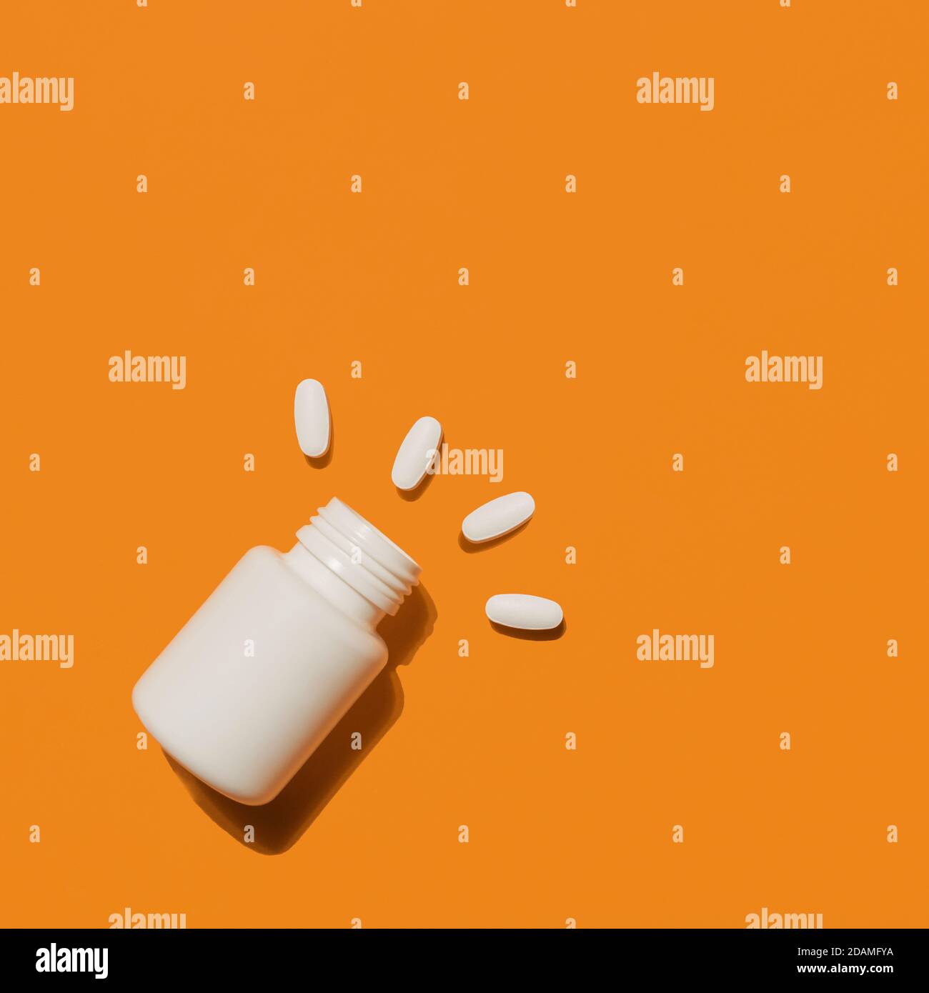 Des pilules et des comprimés médicaux blancs débordent d'une bouteille en plastique. Médecine concepts créatifs. Arrière-plan orange. Vue de dessus de la couche à plat, espace de copie Banque D'Images
