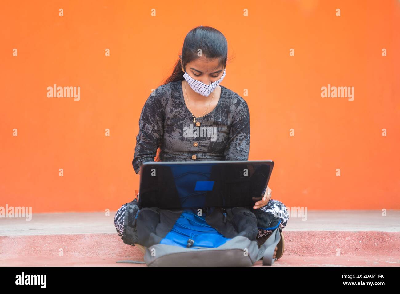 Jeune fille étudiant dans le masque médical occupé à travailler sur ordinateur portable dans le couloir d'université ou campus d'université - concept de la réouverture d'université, nouvelle normale en raison de Banque D'Images