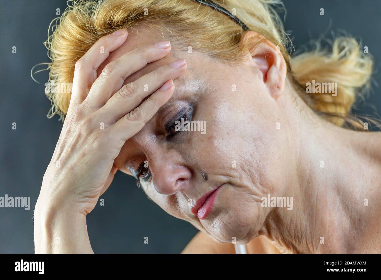 Portrait d'une femme blanche d'âge moyen tenant sa tête d'une main, pleurant avec douleur et désespoir, avec un maquillage qui coule sur son visage Banque D'Images