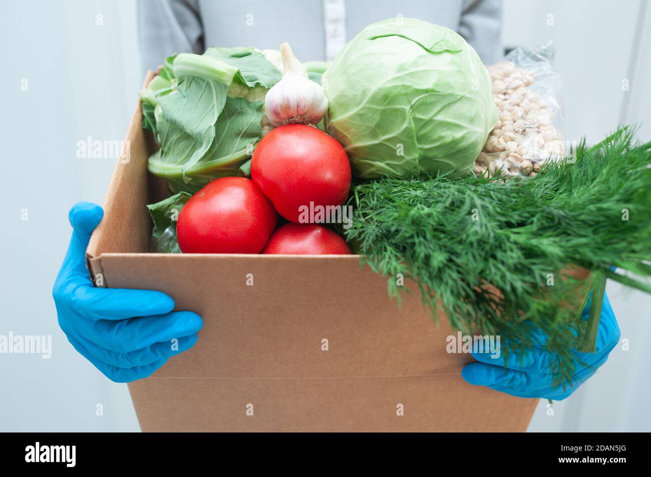 Le volontaire en gants tient la boîte de don de nourriture légumes pour aider les malades ou les pauvres. Donner la boîte avec les denrées alimentaires Banque D'Images