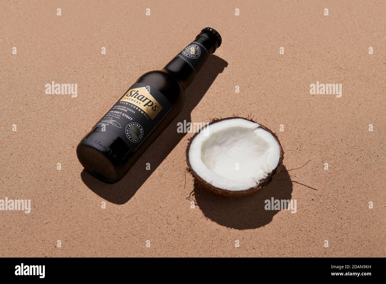 Bière en bouteille piquant de noix de coco de la brasserie Sharps sur du sable avec un noix de coco Banque D'Images