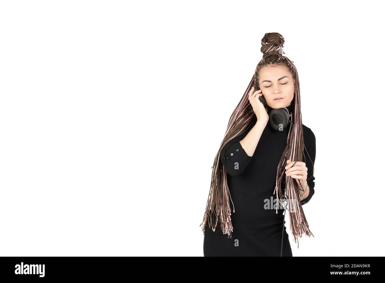 Portrait d'une belle fille avec de longs Afro-braides roses écoutant de la musique dans de grands écouteurs et en se pliant avec élégance. Concept de prise de vue en studio sur fond blanc Banque D'Images