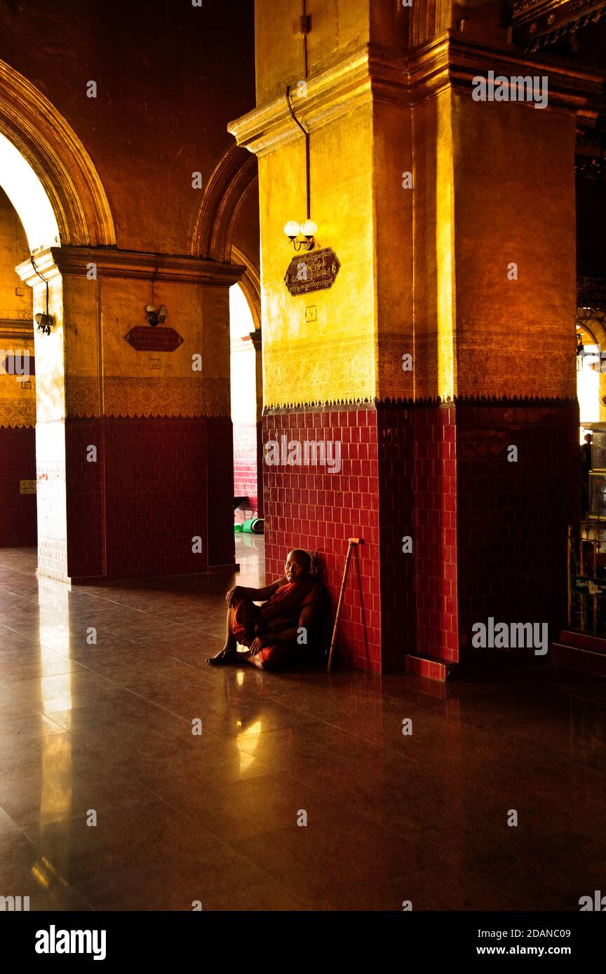 Un vieux moine bouddhiste s'assoit contre le mur dans un Couloir de la Pagode de Mahamuni à Mandalay, au niveau des piliers d'or Banque D'Images