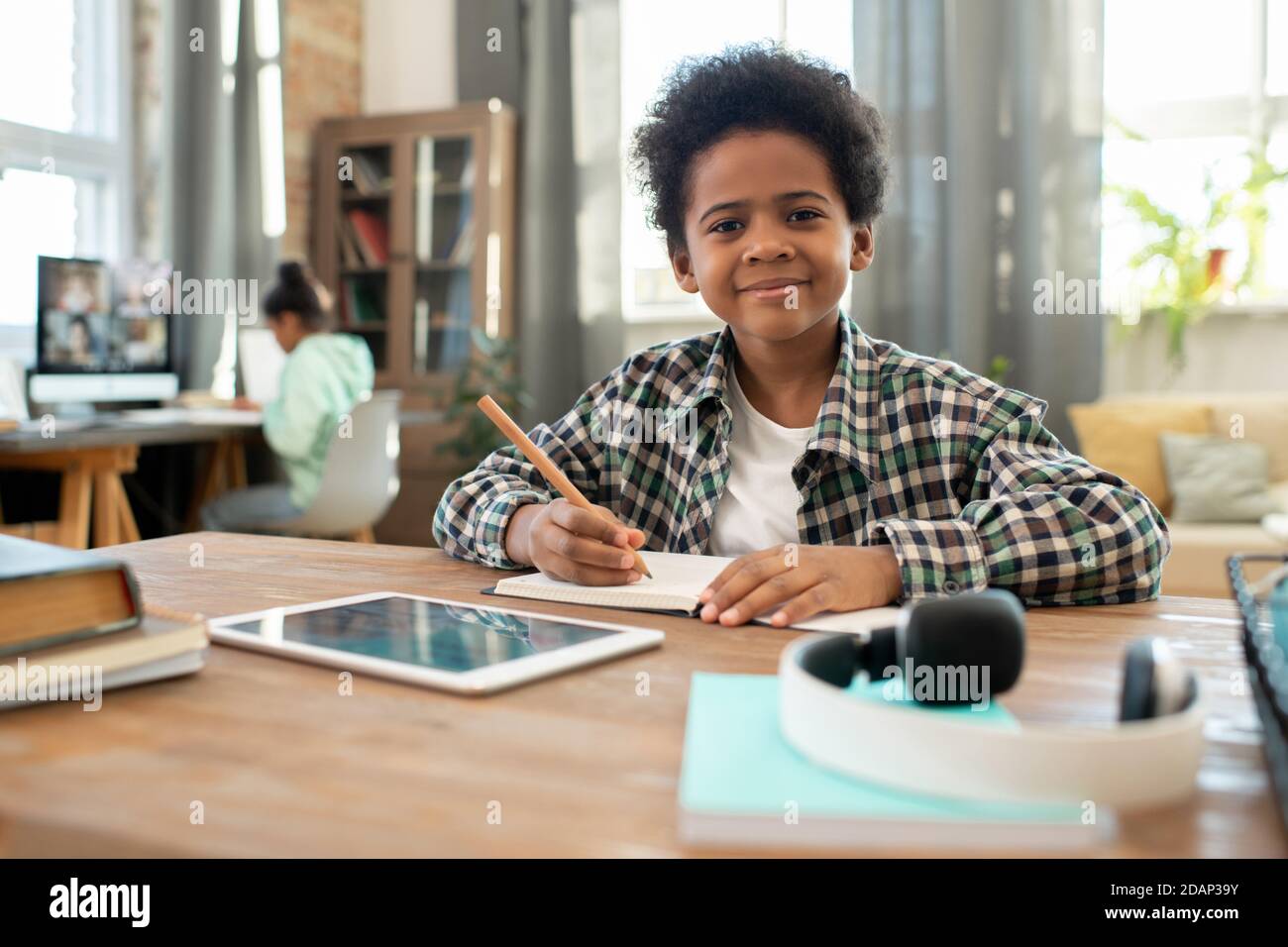 Adorable écolier heureux d'origine africaine vous regardant pendant prendre des notes Banque D'Images