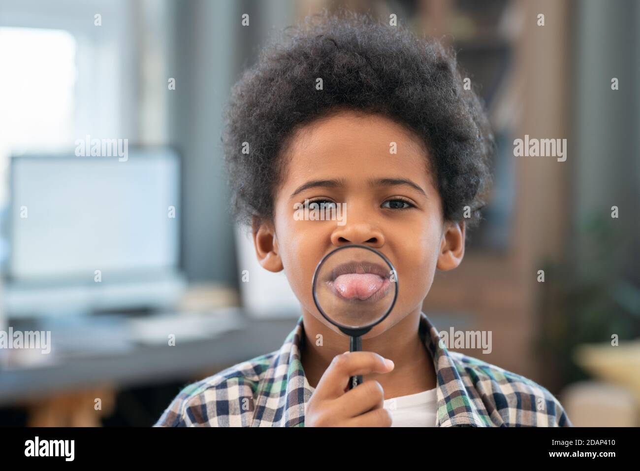 Adorable écolier d'origine africaine tenant une loupe par son enfant bouche Banque D'Images