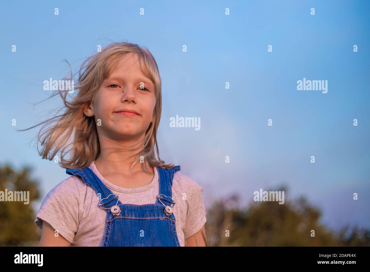 Portrait d'une fille aux cheveux blonds dans une combinaison en denim contre un ciel bleu. Banque D'Images