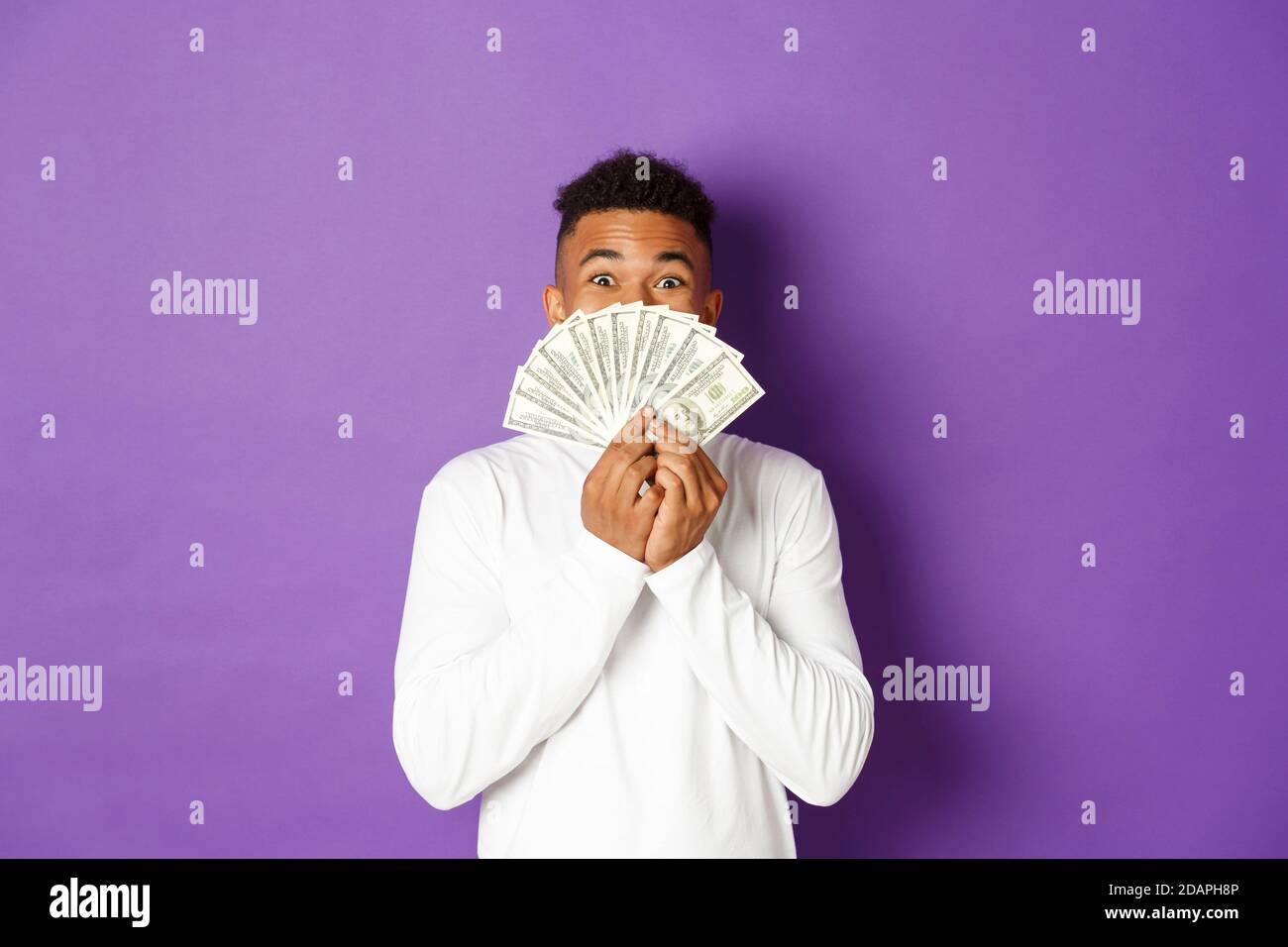 Image d'un homme afro-américain heureux et excité, montrant une grande somme d'argent et se réjouissant, gagnant loterie, debout sur fond violet Banque D'Images