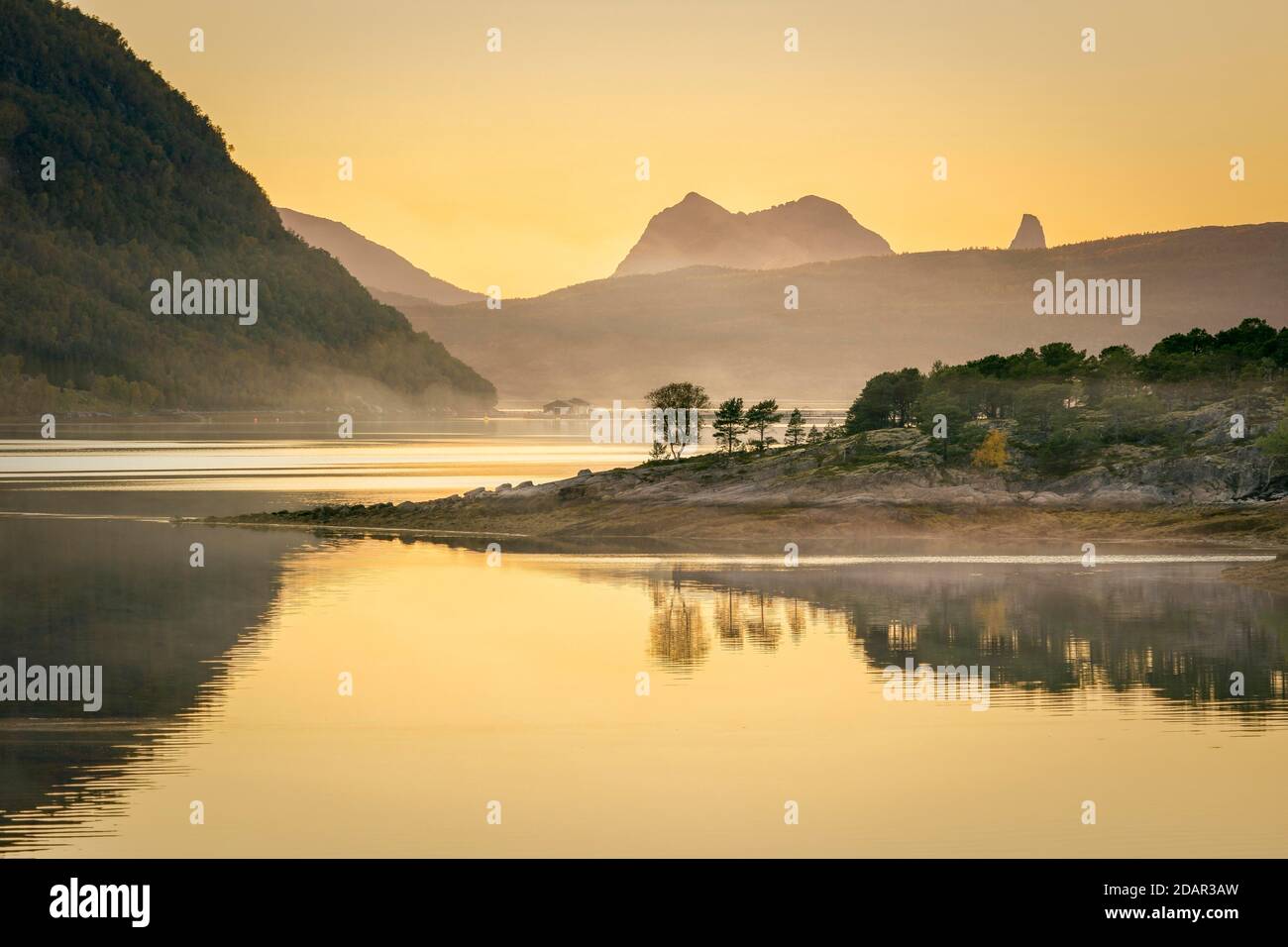 Fjord dans la lumière du soir dans la brume, en face de l'île avec forêt boréale, dans les montagnes arrière, Innhavet, Nordland, Norvège Banque D'Images